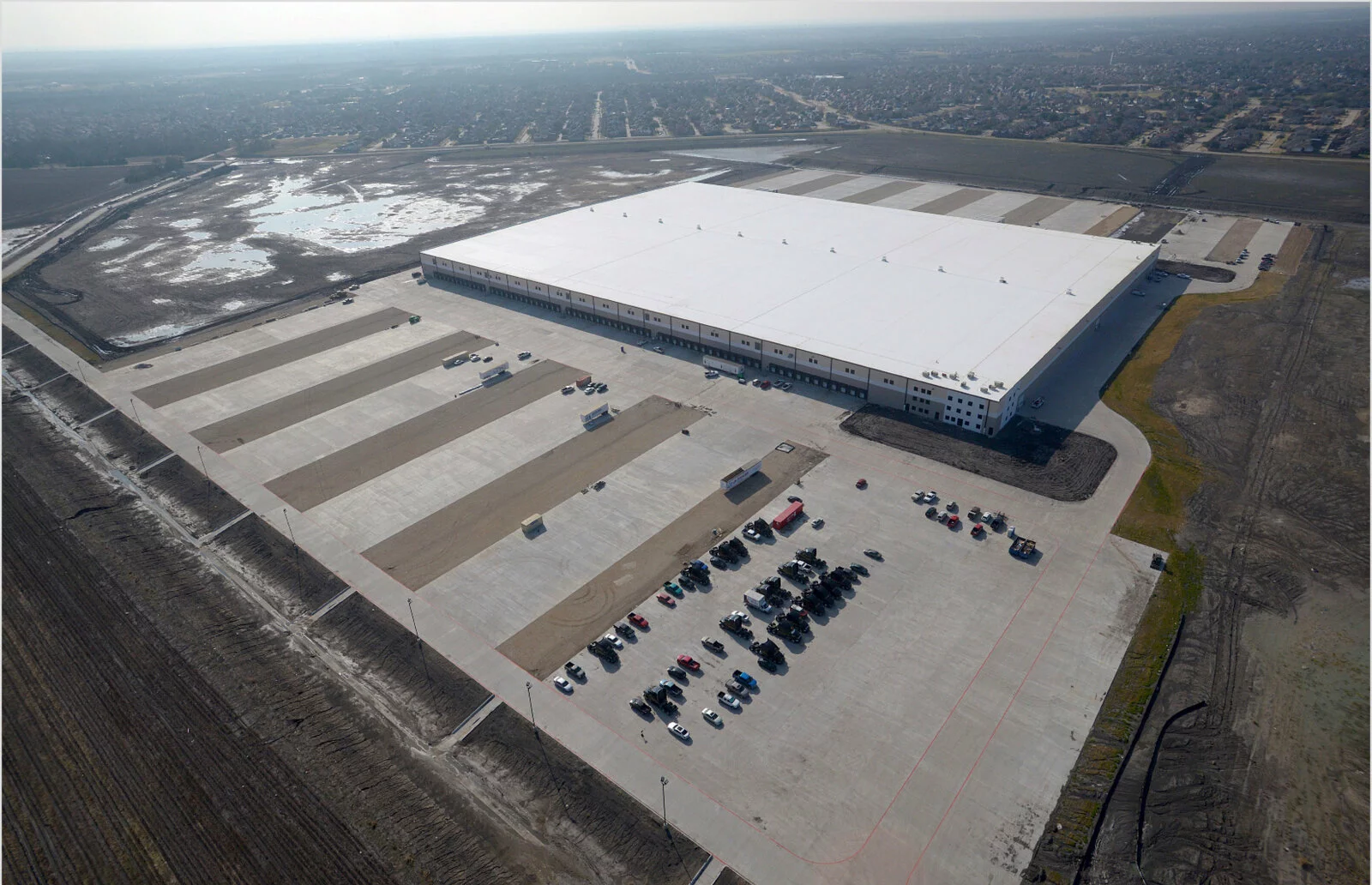 Aerial Exterior of Ashley Furniture warehouse, sprawling landscape in the background, parking around facility, photo taken on a sunny day with minor fog.