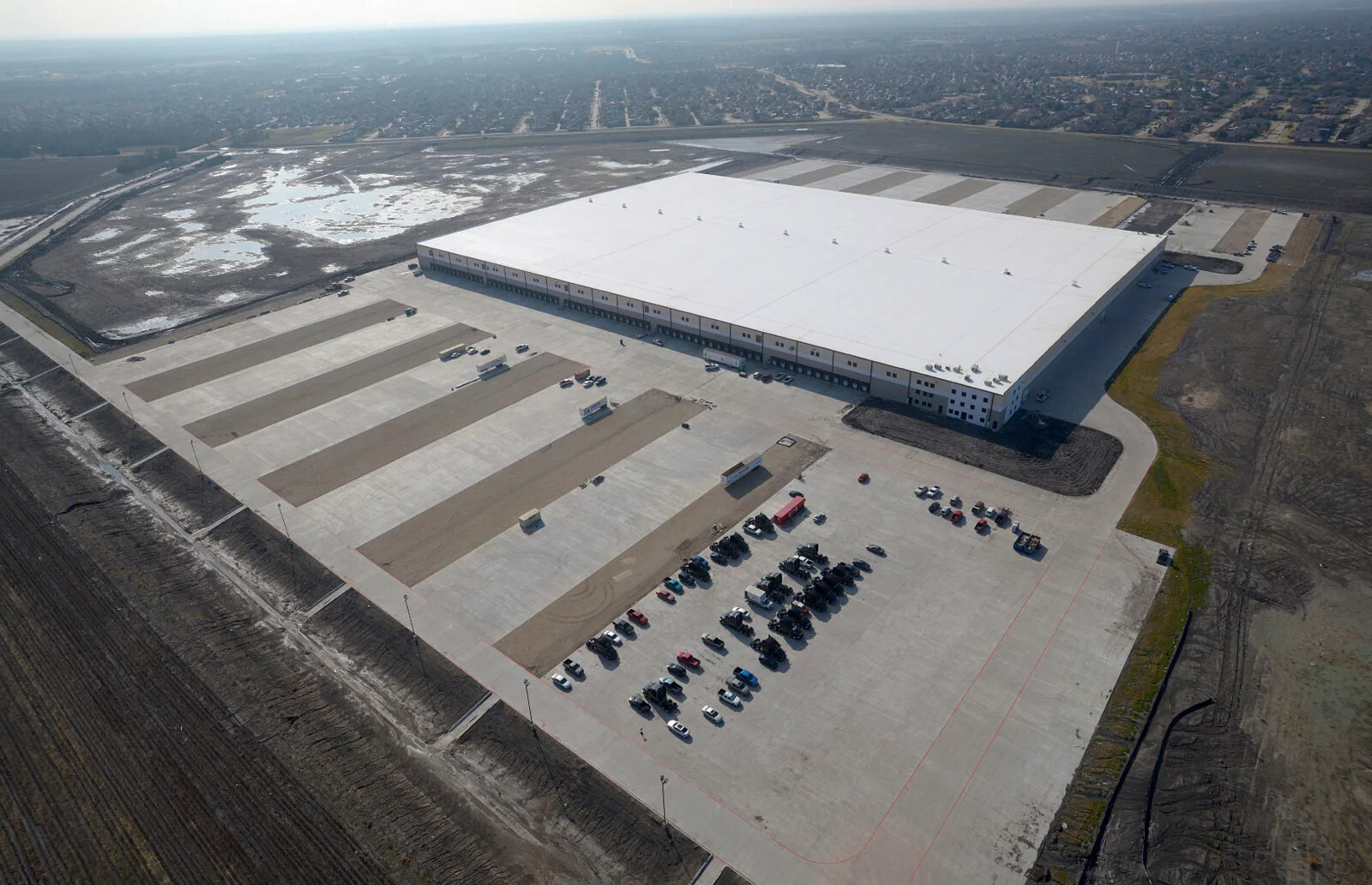 Ashley furniture aerial view, parking lot, city in distance, sunny day, trucks in loading bays.