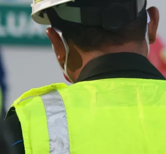 Close up photo of construction worker wearing a High Visibility Vest and a white hard hat.