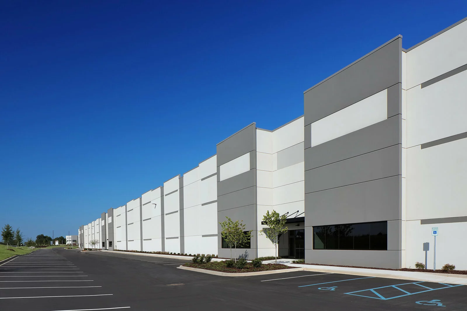 Exterior photo of warehouse, gray and white walls, parking in front, photo taken on a sunny day.
