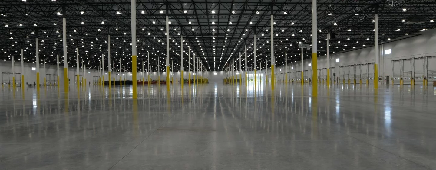 Interior Warehouse/Distribution center, yellow and white load bearing pillars, cement floor, distribution bays on the right side of the photo, vast empty warehouse.