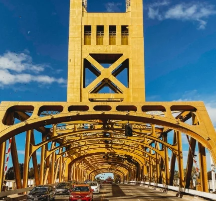 Photo of cars driving under a yellow bridge, photo taken on a sunny day.