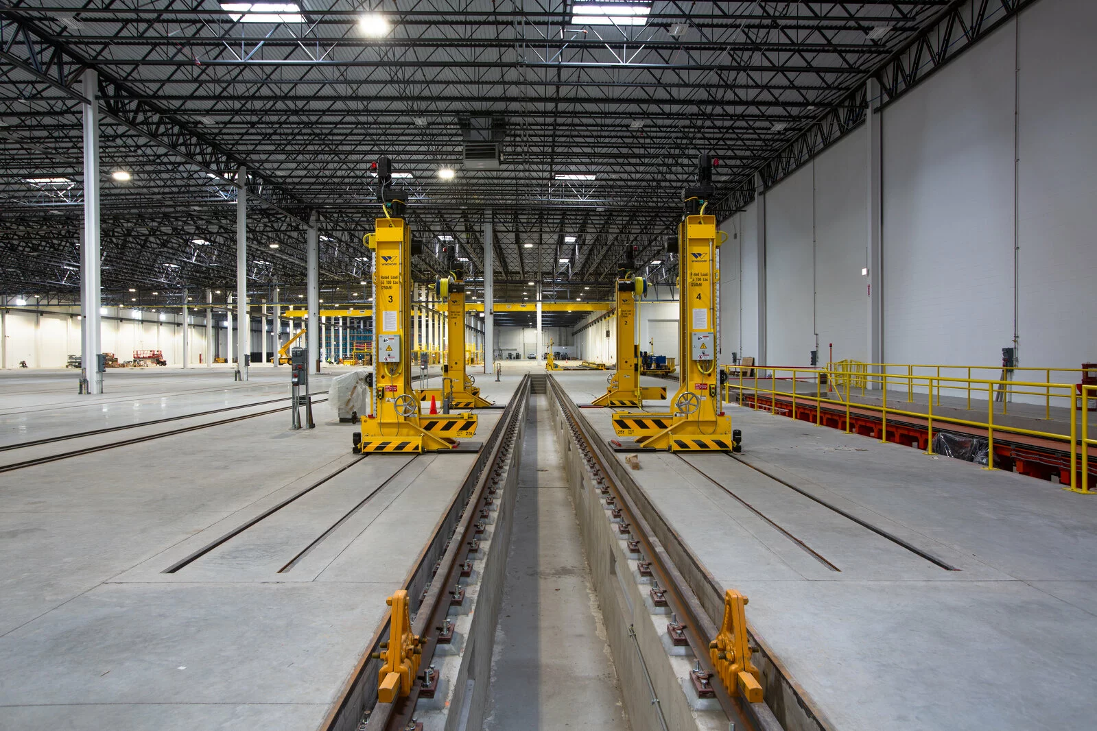 Interior CRRC Warehouse, rail tracks, specialized machinery, vast empty warehouse, concrete floor, white walls, high ceilings.