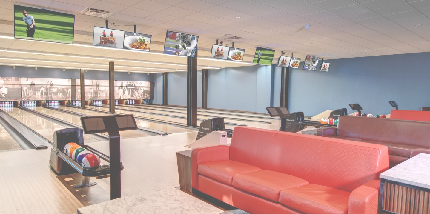 Interior Bowling alley, red couches near lanes, bowling lanes, tv monitors above bowling lanes.