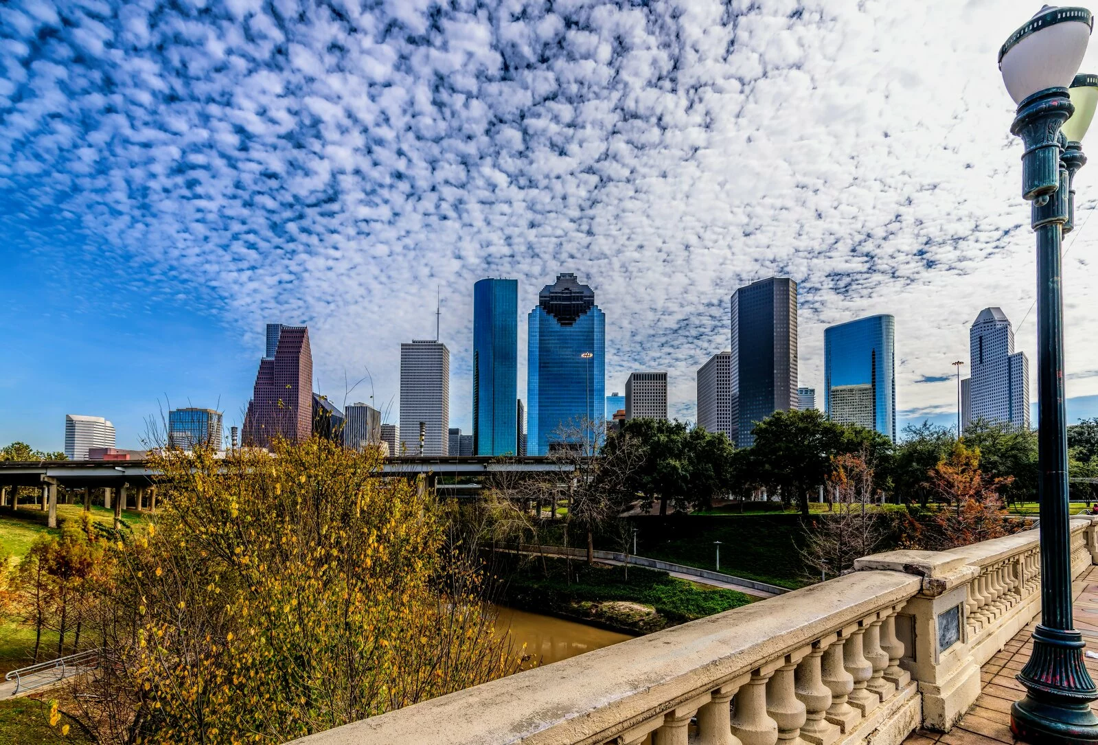 landscape photo of the Houston skyline, photo taken from a bridge, skyscrapers in background, photo taken on a sunny day with clouds.