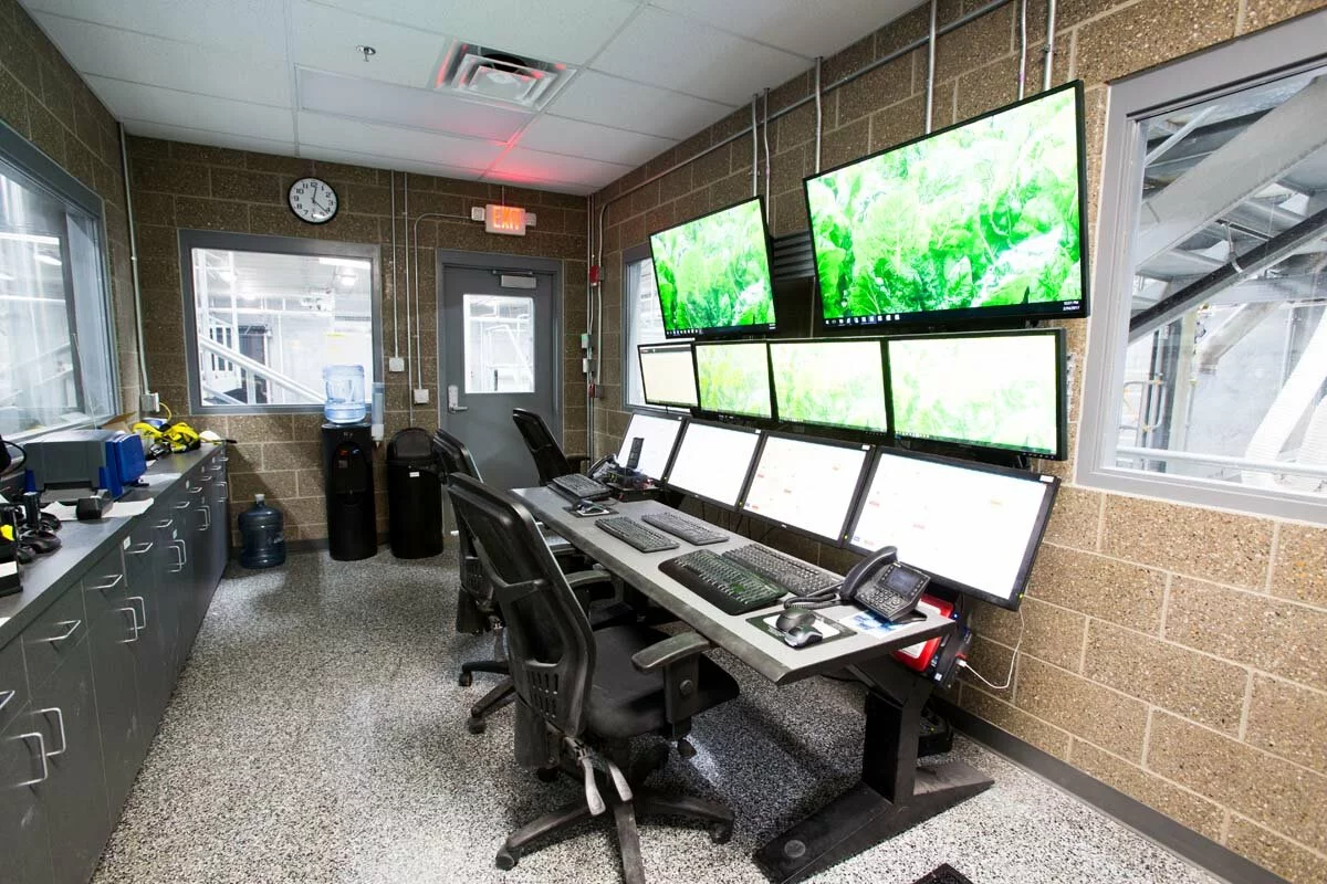 Interior Control room, 10 computer monitors, 6 keyboards, 3 computer chairs, water cooler, speckled floor, brick walls.