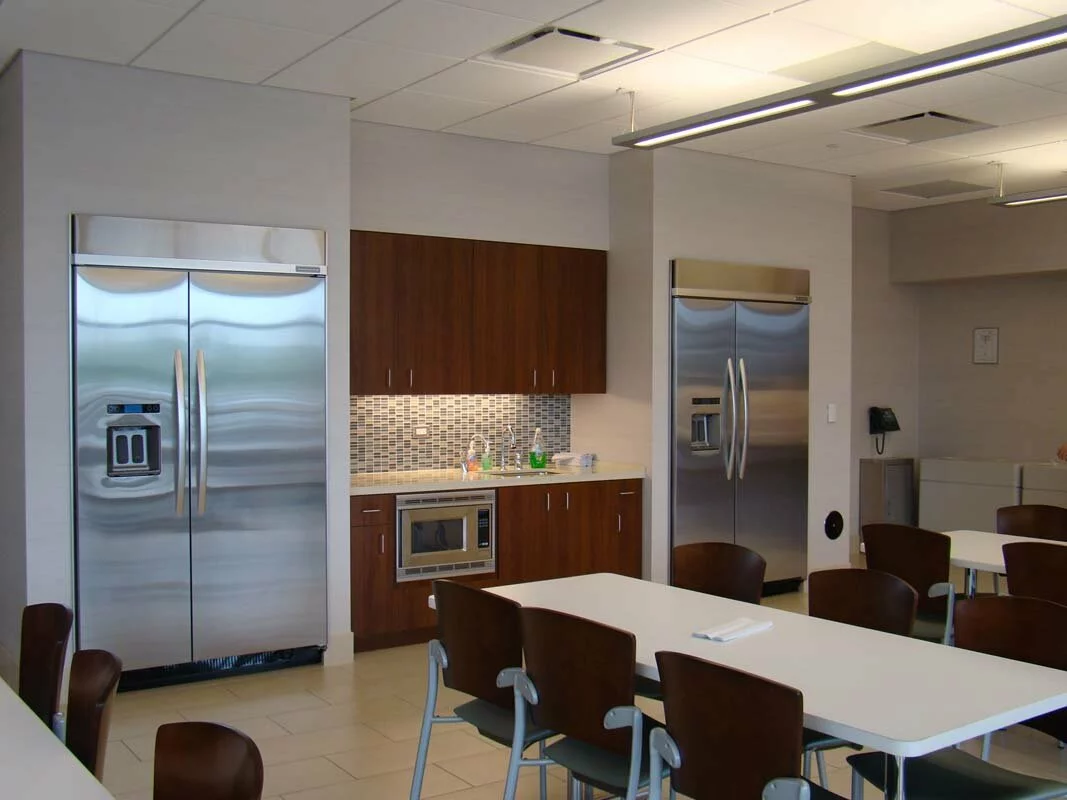 Michael Lewis interior kitchen room, 2 refrigerators, sink, cabinets, microwave, and lunch tables.