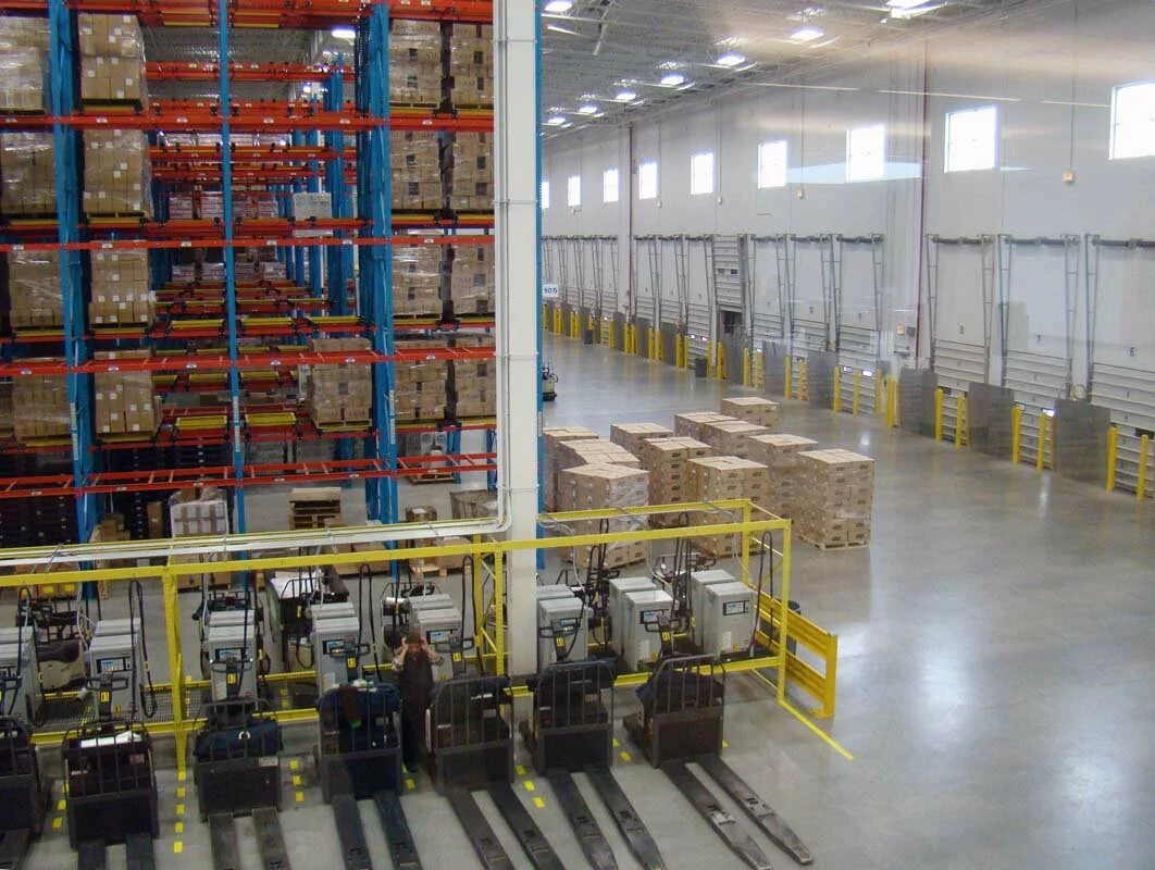 Michael Lewis interior, blue and red shelving, loading bays, product stacks, warehouse machinery.