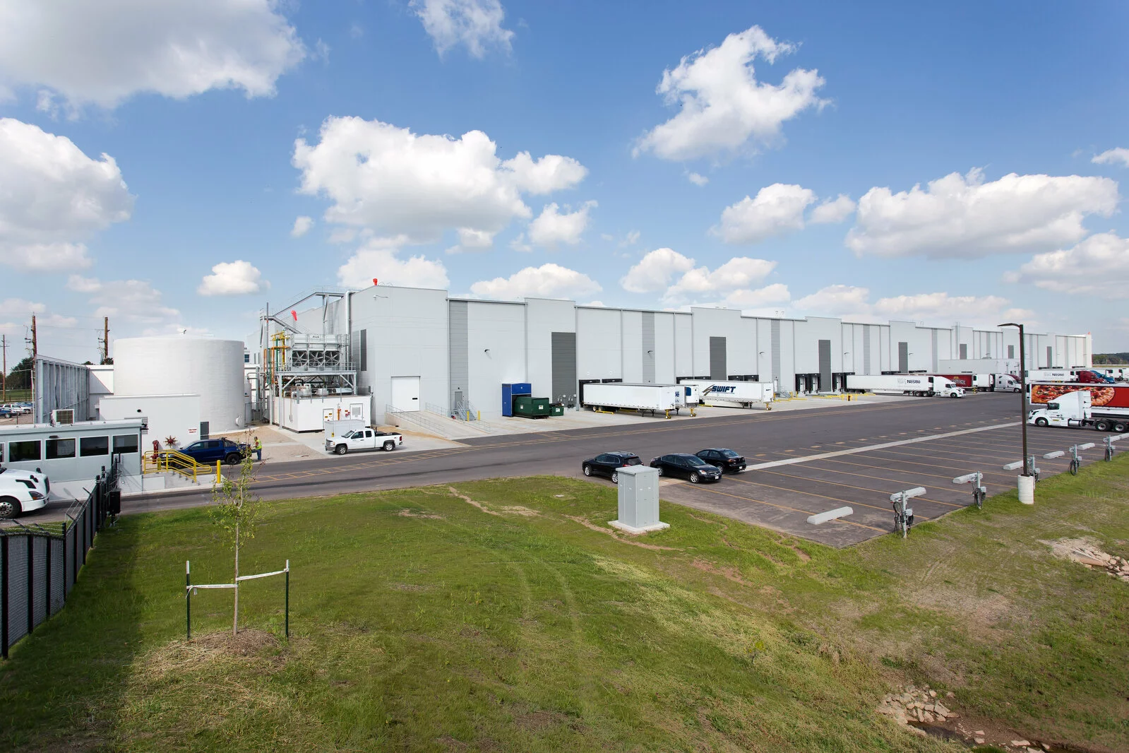 Exterior Nestle Facility, distribution bays, parking in front of facility, photo taken on a sunny day with clouds.
