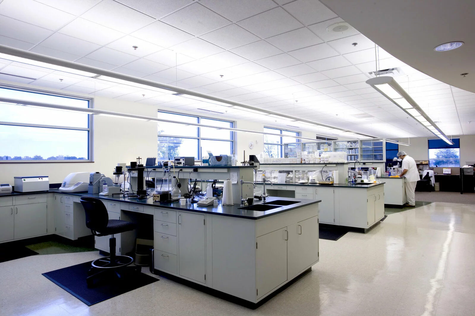Interior Tate & Lyle Science lab, workstations, double sinks at each workstation, beakers, employee performing a task in background, white room with tile floor.