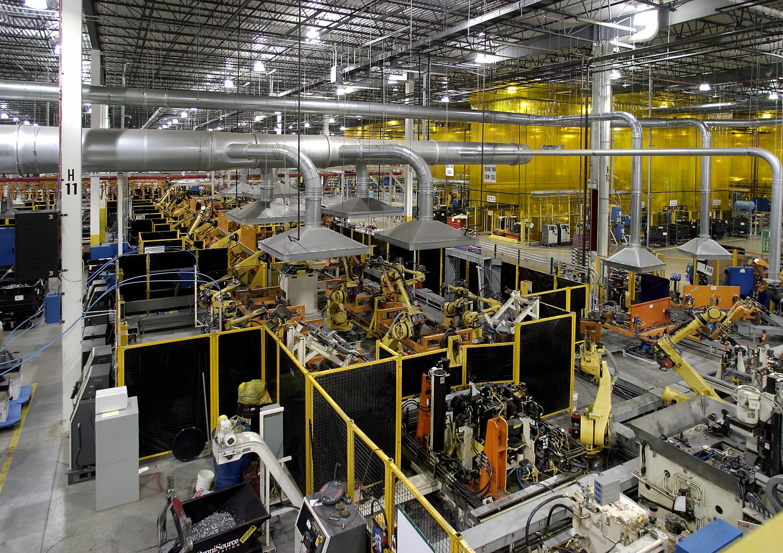 Interior manufacturing facility, robotic assembly line, overhead vents, extremely vast building, yellow floor to ceiling walls in background for specific manufacturing process.