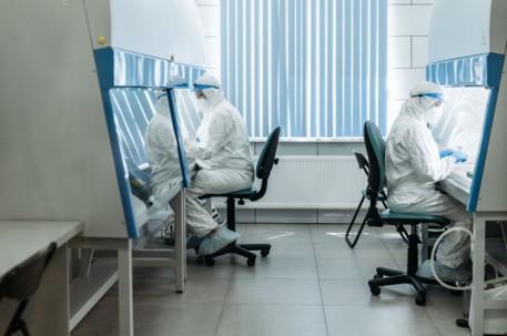 Laboratory technicians wearing full protective equipment working in a cleanroom facility.