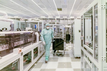 Technician in a full protective bunny suit pushing equipment inside a high-tech cleanroom facility.